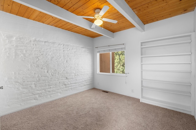 carpeted empty room featuring beamed ceiling, ceiling fan, brick wall, and wood ceiling