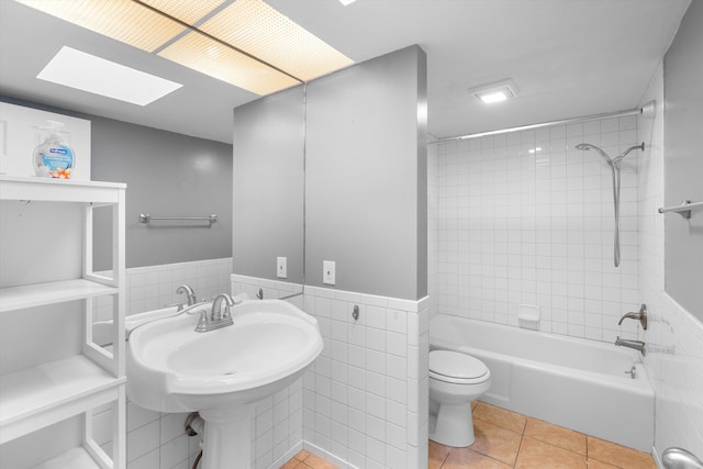 bathroom featuring tile walls, tiled shower / bath combo, a skylight, tile patterned floors, and toilet