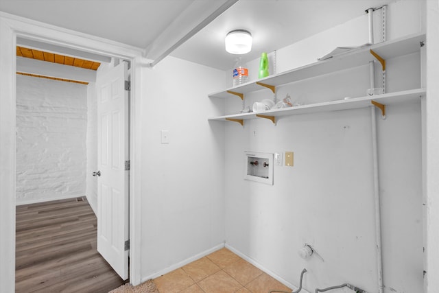 washroom featuring hookup for a washing machine, light tile patterned flooring, and brick wall