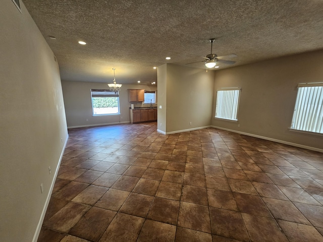 unfurnished living room featuring sink, ceiling fan with notable chandelier, a textured ceiling, and dark tile patterned floors