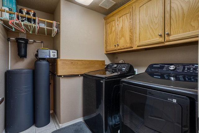 clothes washing area with cabinets, light tile patterned floors, and washer and clothes dryer