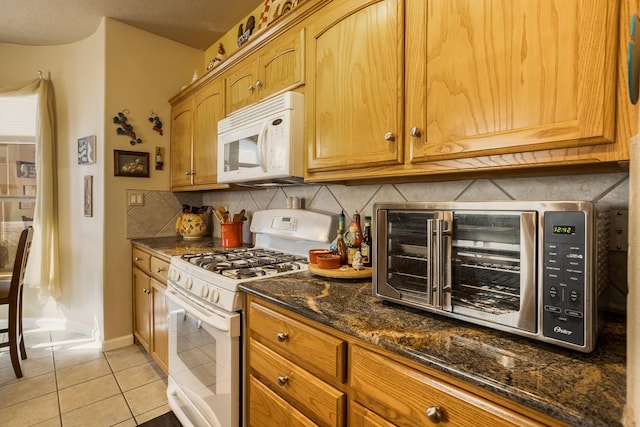 kitchen with tasteful backsplash, light tile patterned floors, white appliances, and dark stone countertops