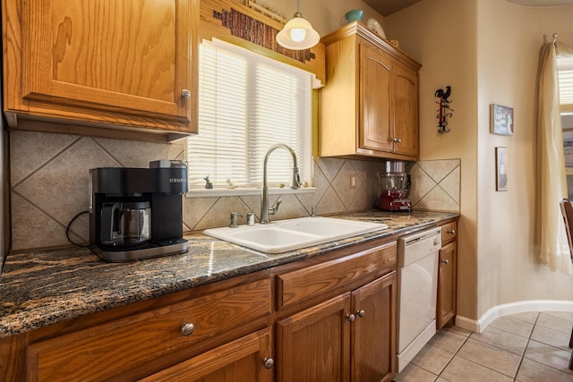 kitchen featuring pendant lighting, dishwasher, sink, dark stone counters, and light tile patterned floors