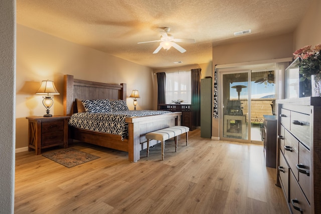 bedroom with access to exterior, light hardwood / wood-style flooring, a textured ceiling, and ceiling fan