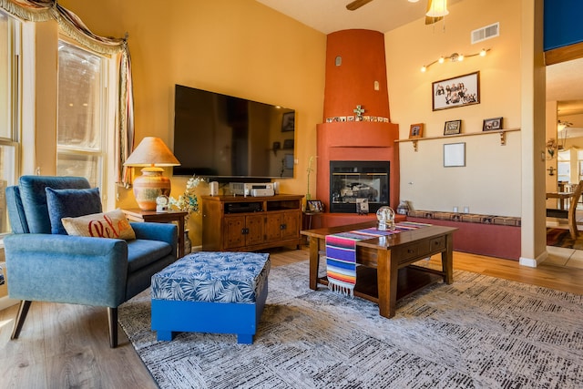 living room featuring wood-type flooring, a towering ceiling, ceiling fan, and a fireplace