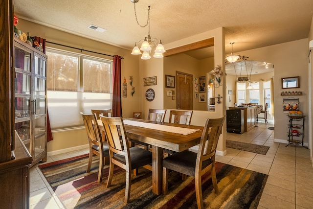 dining space with a notable chandelier, a textured ceiling, and light tile patterned flooring