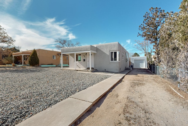 pueblo revival-style home featuring driveway, stucco siding, fence, and an outdoor structure