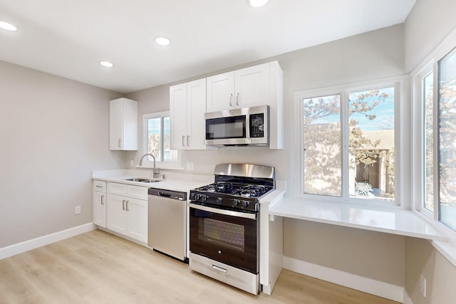 kitchen with light wood-style flooring, stainless steel appliances, a sink, white cabinetry, and baseboards