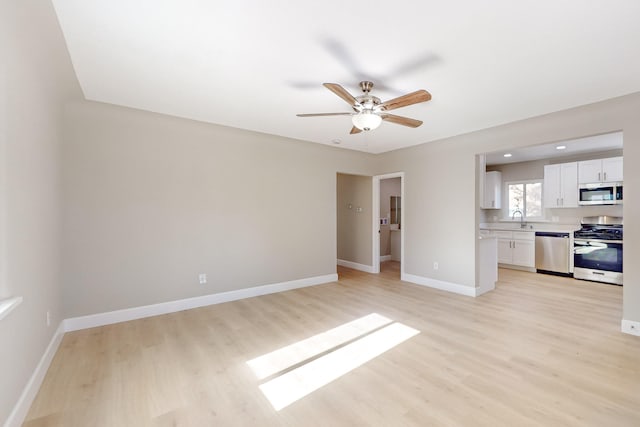 unfurnished living room featuring a ceiling fan, light wood-type flooring, a sink, and baseboards