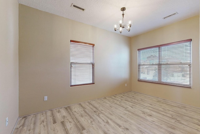 unfurnished room featuring light hardwood / wood-style flooring, a textured ceiling, and a notable chandelier