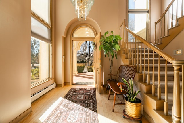 interior space with a baseboard radiator, a chandelier, light hardwood / wood-style floors, and a towering ceiling