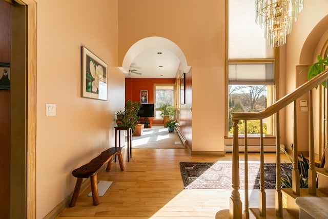 corridor featuring hardwood / wood-style flooring, a baseboard radiator, a chandelier, and a high ceiling