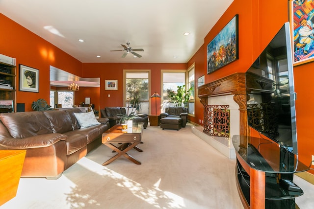 carpeted living room featuring ceiling fan with notable chandelier, a healthy amount of sunlight, and a high end fireplace