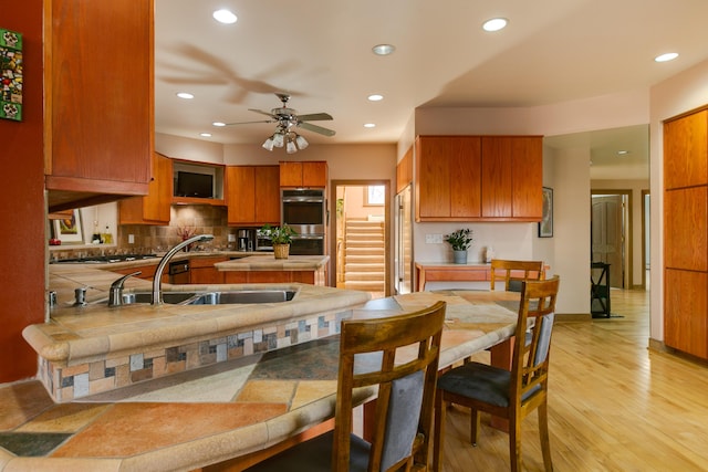 kitchen featuring appliances with stainless steel finishes, sink, decorative backsplash, ceiling fan, and light hardwood / wood-style flooring