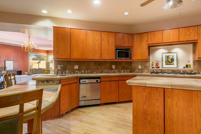 kitchen featuring appliances with stainless steel finishes, ceiling fan with notable chandelier, tasteful backsplash, sink, and light wood-type flooring