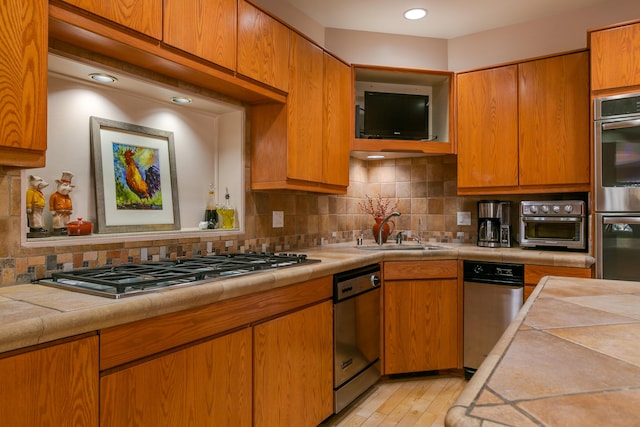 kitchen featuring appliances with stainless steel finishes, sink, decorative backsplash, tile counters, and light wood-type flooring