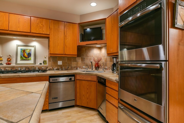 kitchen featuring sink, stainless steel appliances, light hardwood / wood-style floors, decorative backsplash, and tile countertops