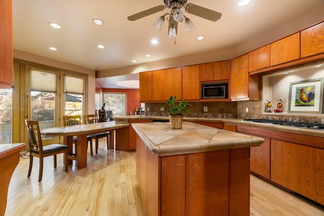 kitchen featuring a center island, tasteful backsplash, tile counters, built in microwave, and stainless steel gas stovetop