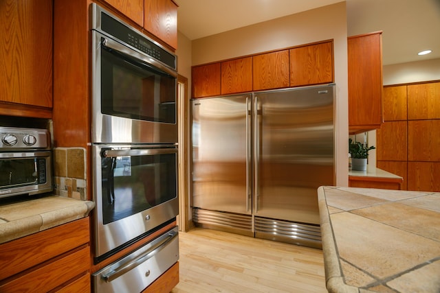 kitchen featuring light hardwood / wood-style flooring, tile counters, and stainless steel appliances