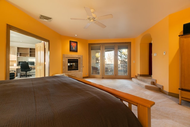 unfurnished bedroom with light colored carpet, access to outside, a tile fireplace, and ceiling fan