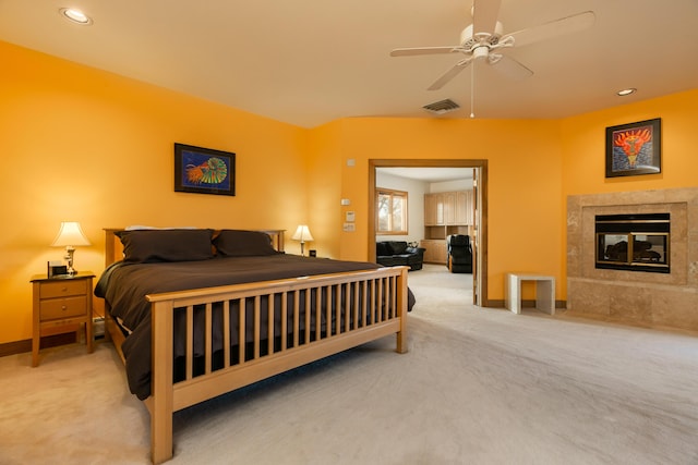 carpeted bedroom featuring a tiled fireplace and ceiling fan