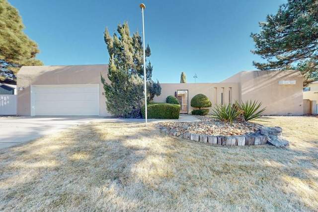 pueblo-style house featuring a garage and a front lawn