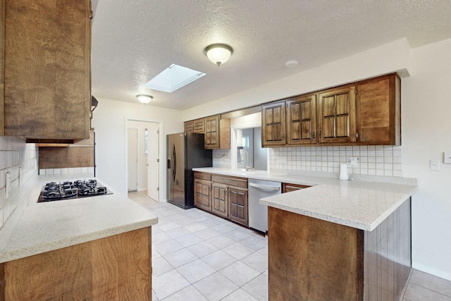 kitchen featuring a skylight, black appliances, sink, kitchen peninsula, and light stone countertops