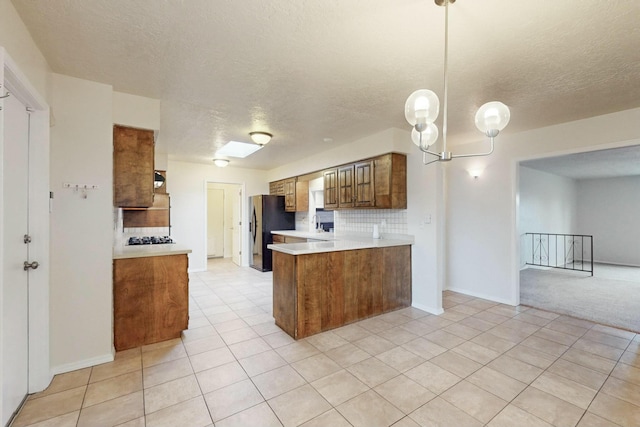 kitchen featuring decorative light fixtures, decorative backsplash, stainless steel gas cooktop, kitchen peninsula, and black fridge