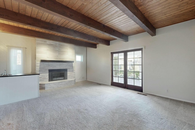 unfurnished living room with wood ceiling, a stone fireplace, beamed ceiling, and a healthy amount of sunlight