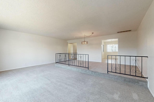 carpeted empty room with a textured ceiling and a chandelier