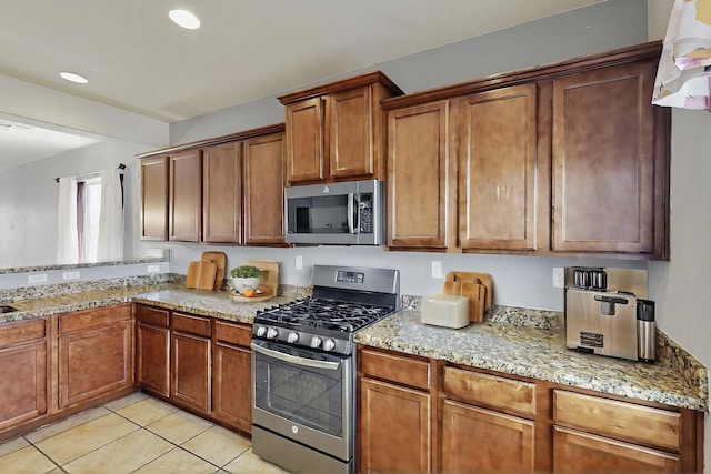 kitchen featuring brown cabinetry, light tile patterned flooring, light stone countertops, recessed lighting, and appliances with stainless steel finishes
