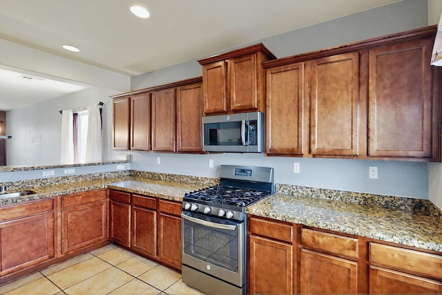 kitchen with appliances with stainless steel finishes, brown cabinets, light tile patterned floors, light stone counters, and recessed lighting