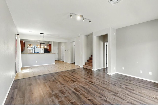unfurnished living room with visible vents, wood finished floors, baseboards, a chandelier, and stairs