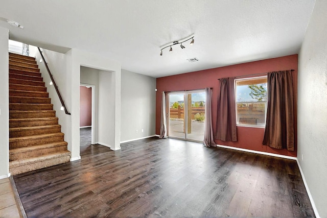 unfurnished living room featuring track lighting, dark wood-style flooring, stairs, and visible vents