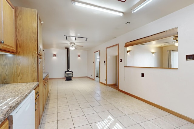 kitchen featuring ceiling fan, light tile patterned flooring, light countertops, dishwasher, and a wood stove