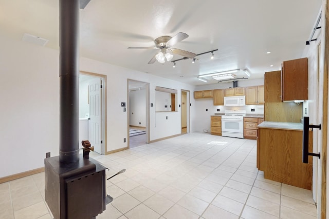 kitchen with ceiling fan, white appliances, baseboards, light countertops, and a wood stove