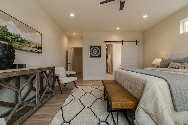 bedroom with a barn door, recessed lighting, light wood-style flooring, baseboards, and ceiling fan
