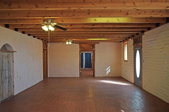 empty room featuring beam ceiling, ceiling fan, and brick wall