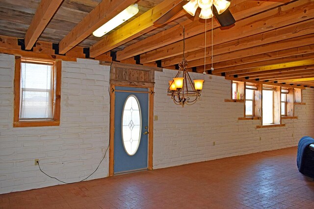 entryway featuring brick wall, beam ceiling, and ceiling fan with notable chandelier