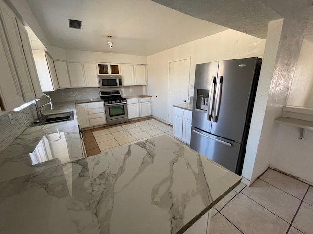 10613 Benavides Rd SW, Albuquerque, NM 87121 - kitchen with appliances with stainless steel finishes, a sink, light stone counters, white cabinetry, and backsplash