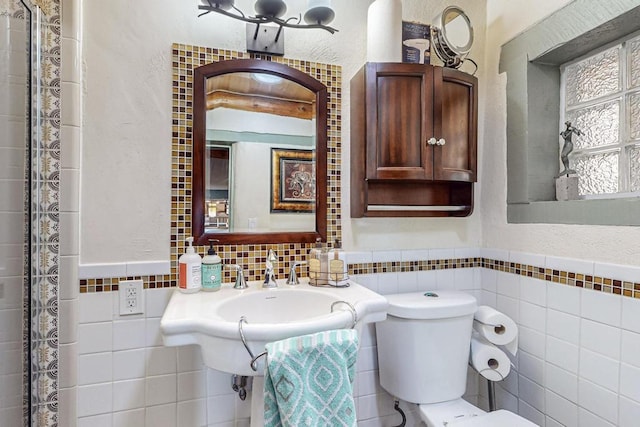 bathroom featuring wainscoting, a textured wall, tile walls, and toilet