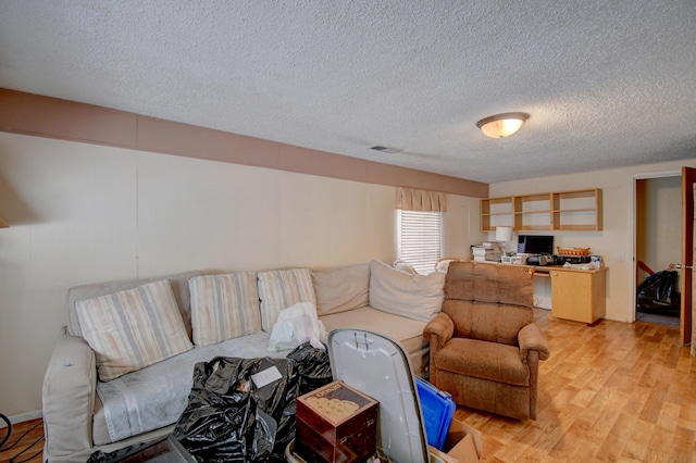 living room with built in desk, light hardwood / wood-style flooring, and a textured ceiling