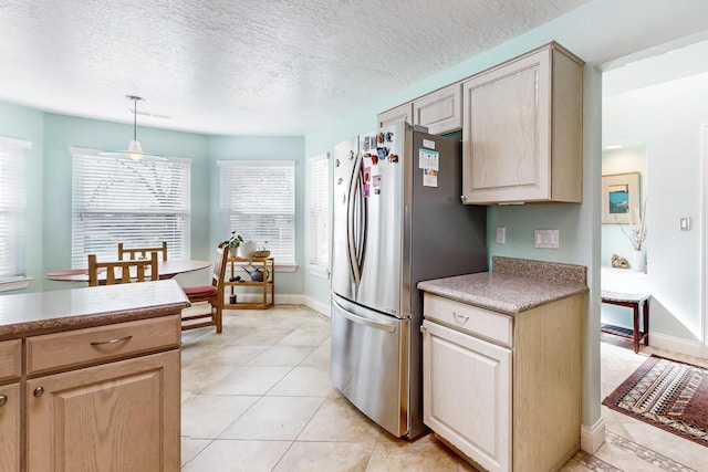 kitchen featuring pendant lighting, stainless steel fridge, light tile patterned floors, light brown cabinets, and a textured ceiling