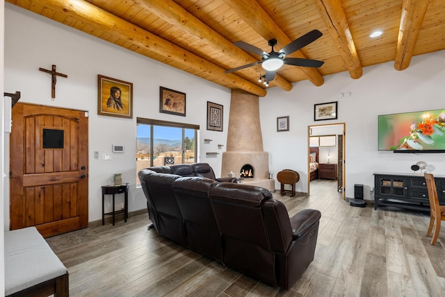 living room with beamed ceiling, wood-type flooring, a wood stove, ceiling fan, and wood ceiling