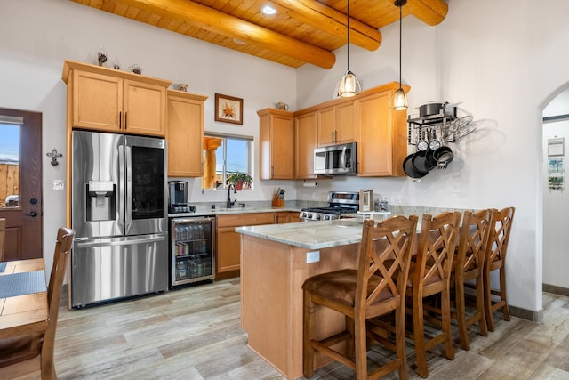 kitchen with sink, wine cooler, hanging light fixtures, light stone counters, and stainless steel appliances