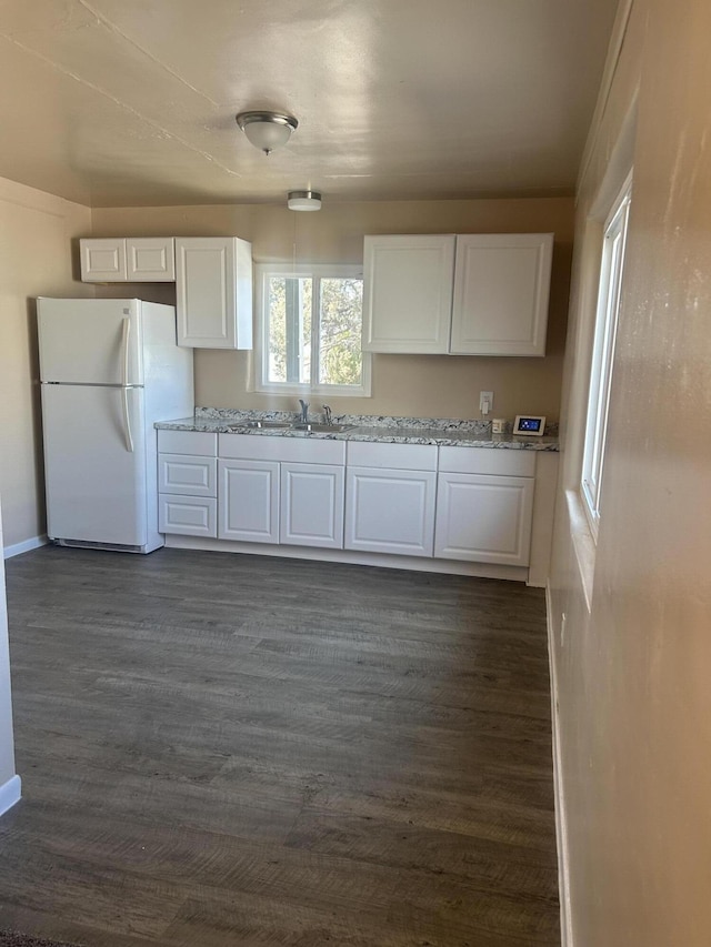 kitchen featuring dark hardwood / wood-style floors, sink, white cabinets, white refrigerator, and light stone countertops