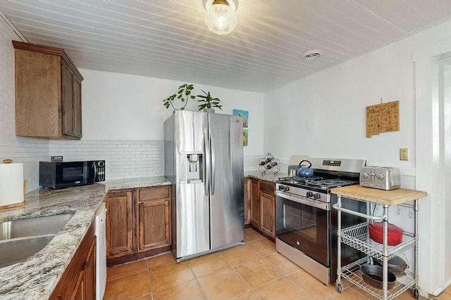 kitchen with sink, light tile patterned floors, stainless steel appliances, light stone countertops, and decorative backsplash