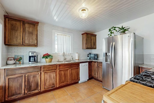 kitchen featuring tasteful backsplash, dishwasher, sink, light stone counters, and stainless steel refrigerator with ice dispenser