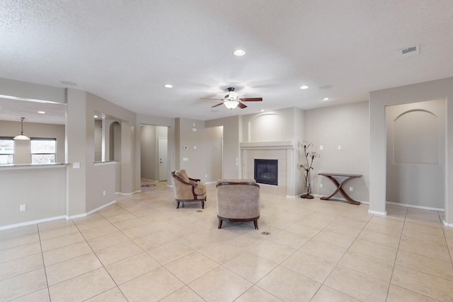 living area featuring light tile patterned floors, a textured ceiling, a tile fireplace, and ceiling fan