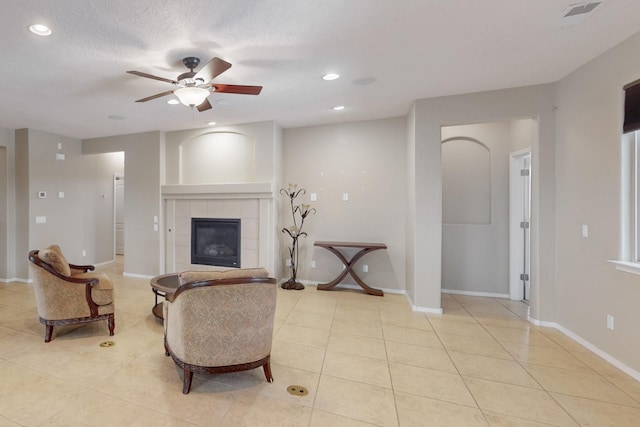 living room with ceiling fan, light tile patterned floors, a textured ceiling, and a fireplace